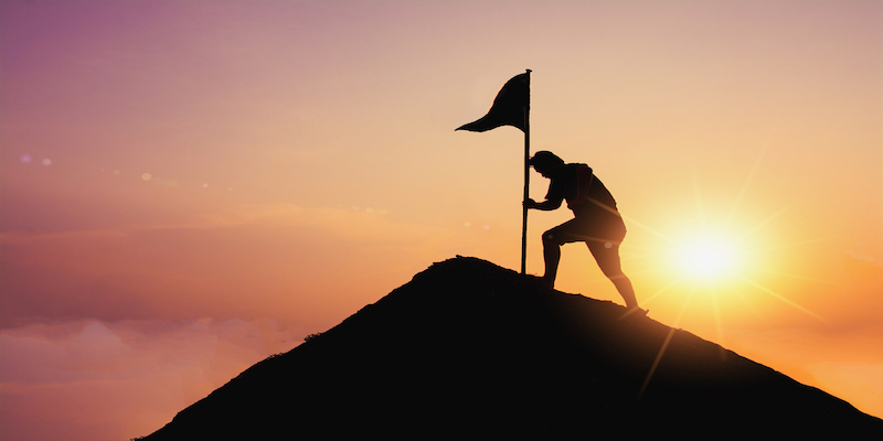 businessman placing flag on mountain